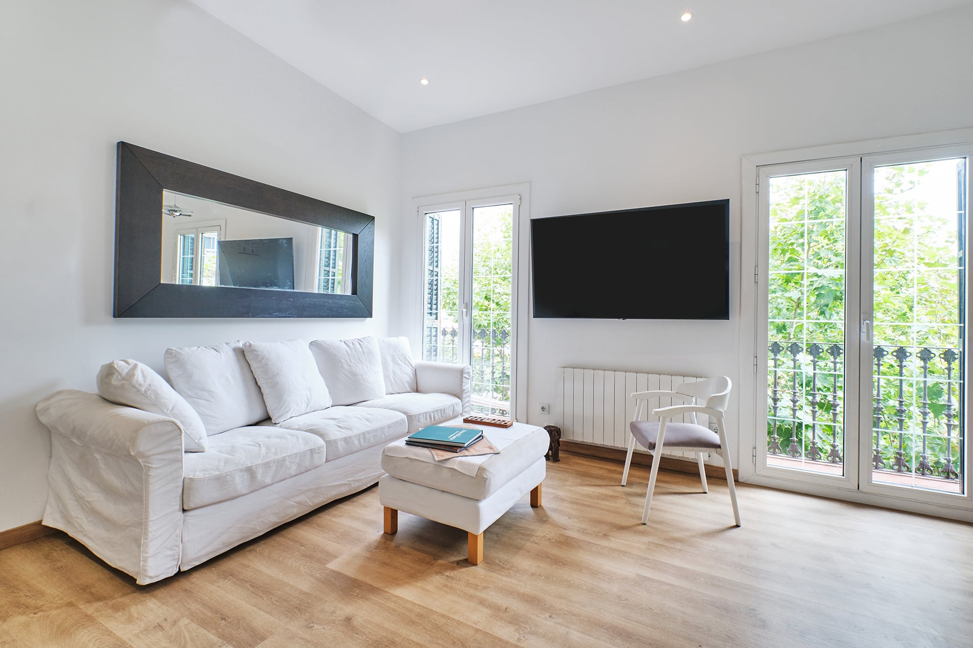 Barcelona roof studio - first floor, living room area with a white couch and ottoman next to two glass doors that open to the balcony, designed by Beatrice Leupold Barcelona roof studio - first floor, living room area with a white couch and ottoman next to two glass doors that open to the balcony, designed by Beatrice Leupold